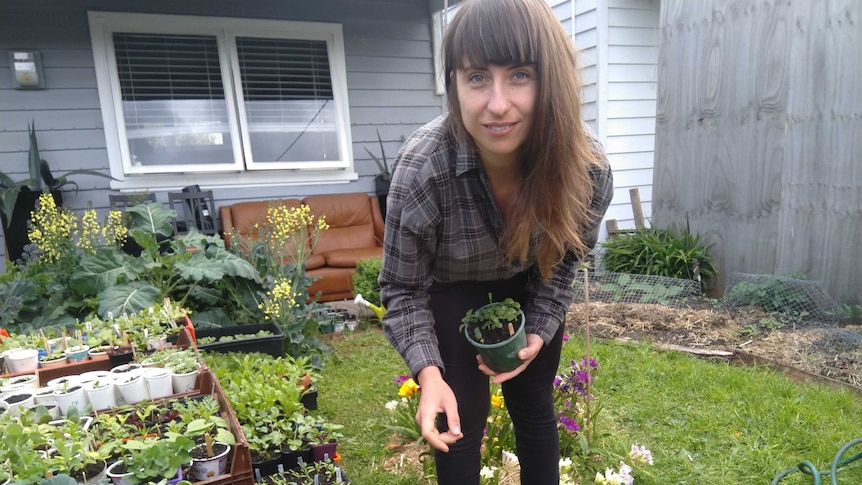 Young woman with long brown hair crouches down next to seedlings in her front garden.