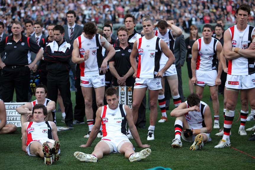 St Kilda AFL players lump on the ground or stand looking downcast in the minutes after an AFL grand final 