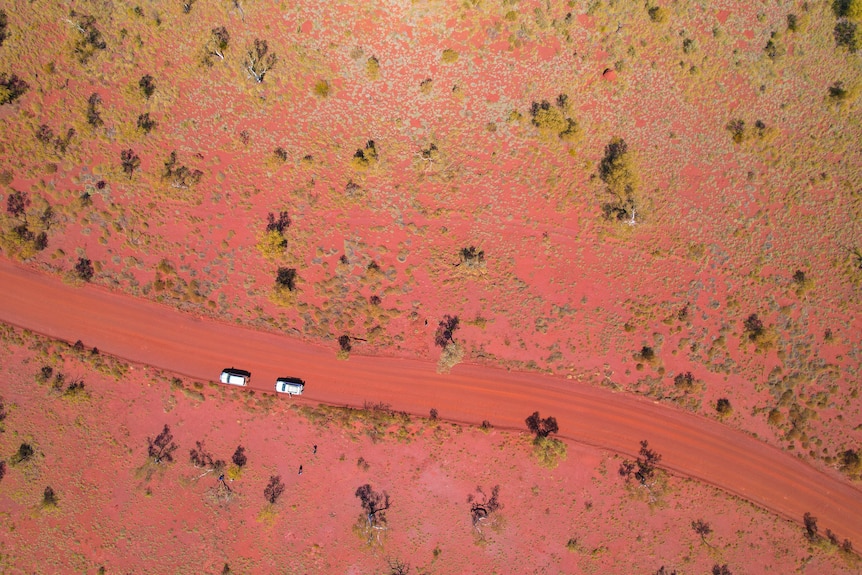 Two vehicles driving in a remote area of the Pilbara surrounded by red earth.  