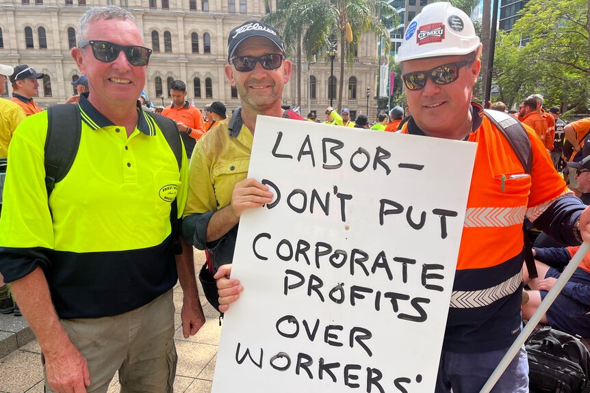 three construction workers hold a sign at the rally 