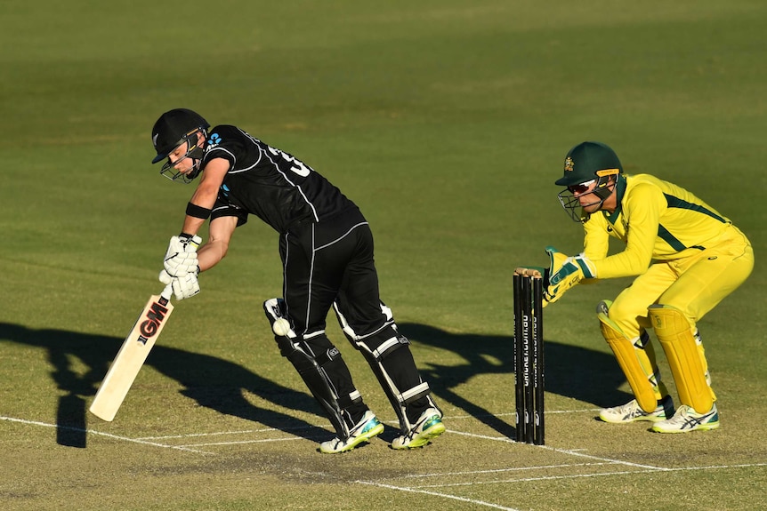 A New Zealand cricketer plays forward to a ball as the wicketkeeper crouches close behind stumps.