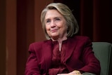 Hillary Clinton wears a burgundy suit and smiles as she sits