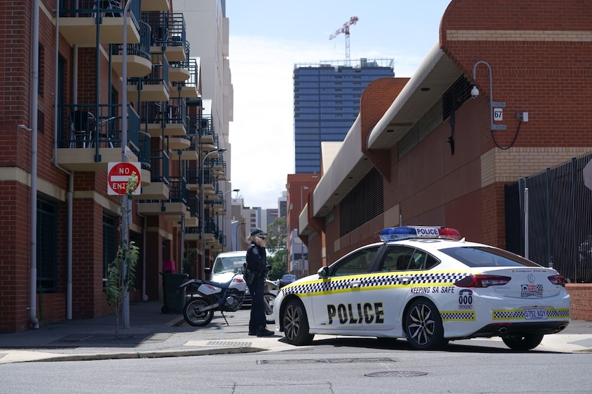 A female police officer stands next to a SAPOL car, outside of the Adelaide Remand Centre