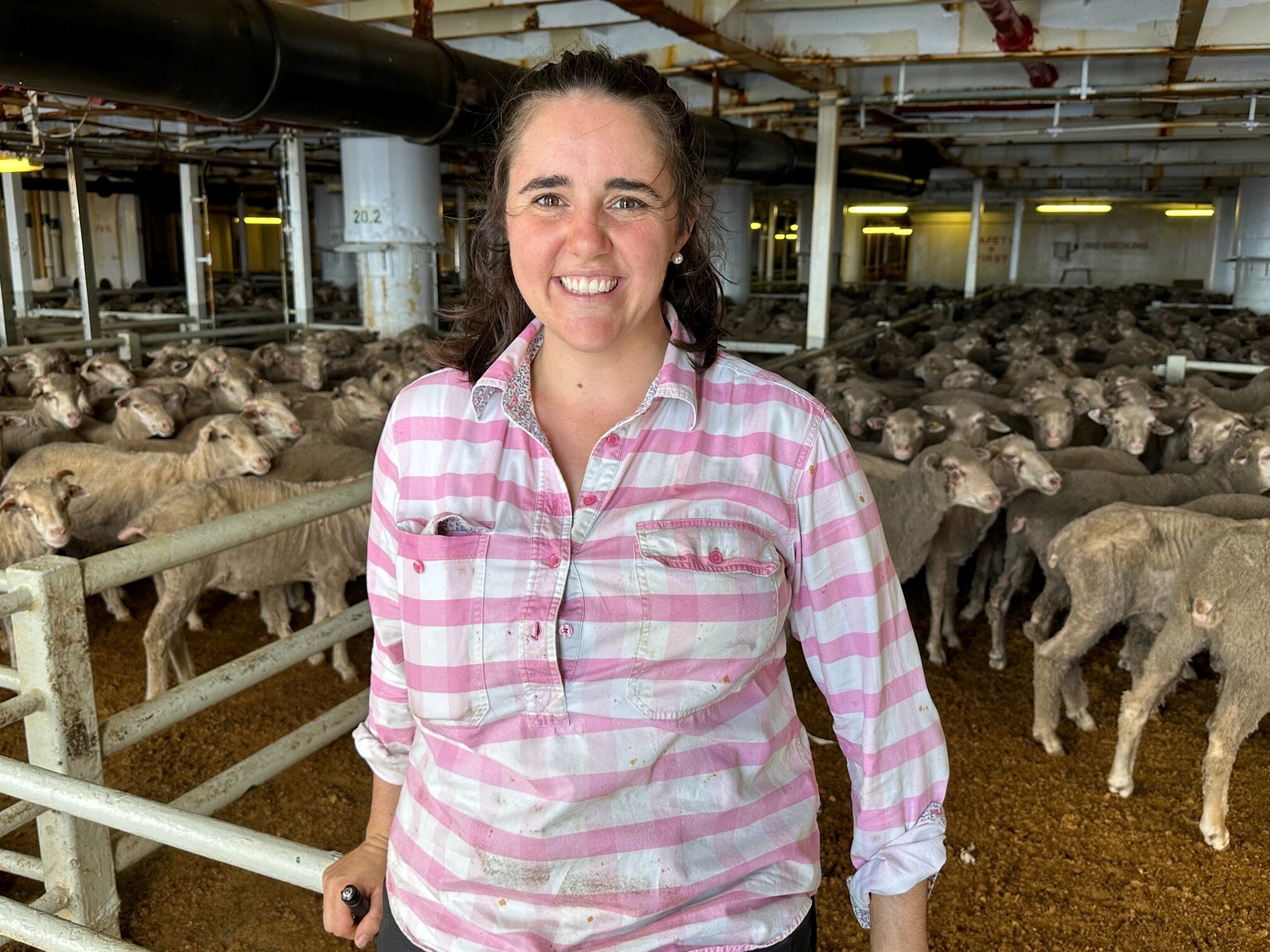 A smiling woman stands in front of sheep in pens.