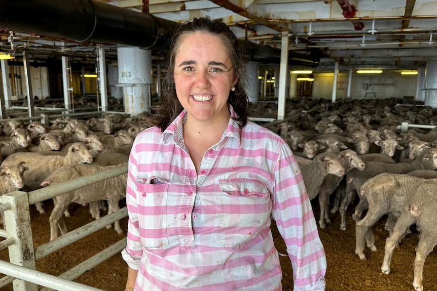 A smiling woman stands in front of sheep in pens.
