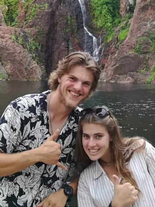 A man and woman smile and pose in front of a waterfall.