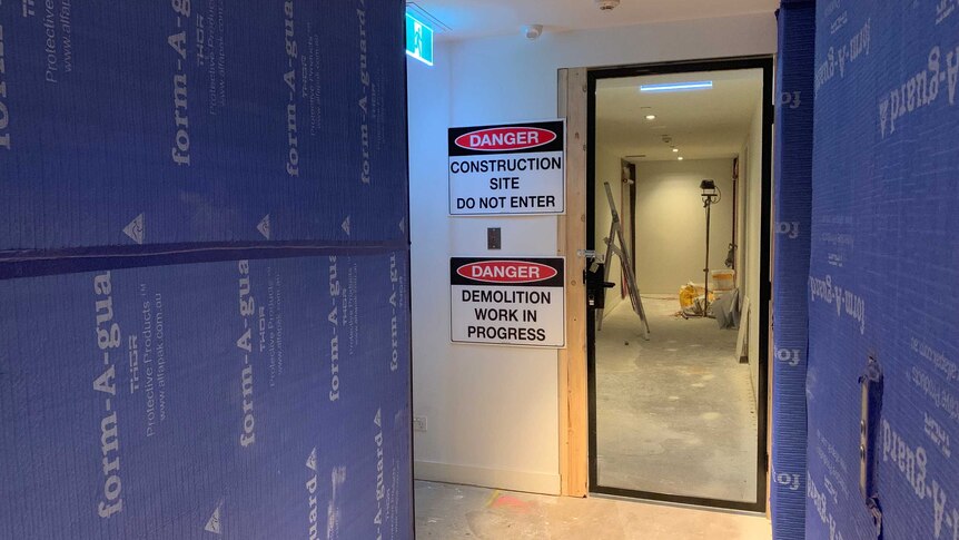 An apartment building corridor with a danger construction site sign beside a door.