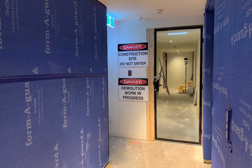 An apartment building corridor with a danger construction site sign beside a door.