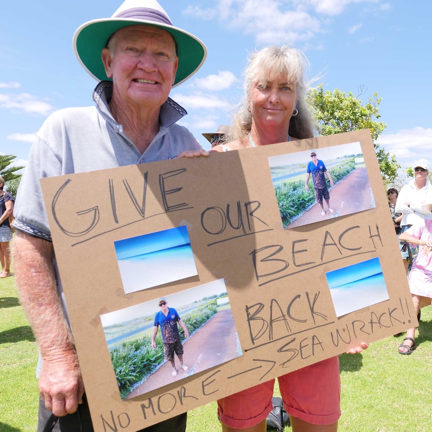 A man and a woman holding a sign saying 'Give our beach back'