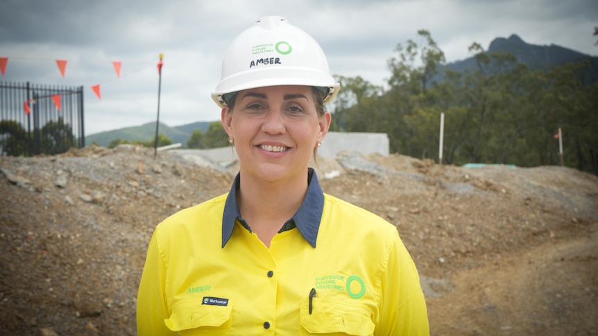 A woman stands in front of a camera on a construction site smiling