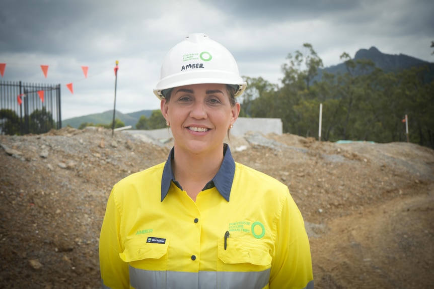 A woman stands in front of a camera on a construction site smiling