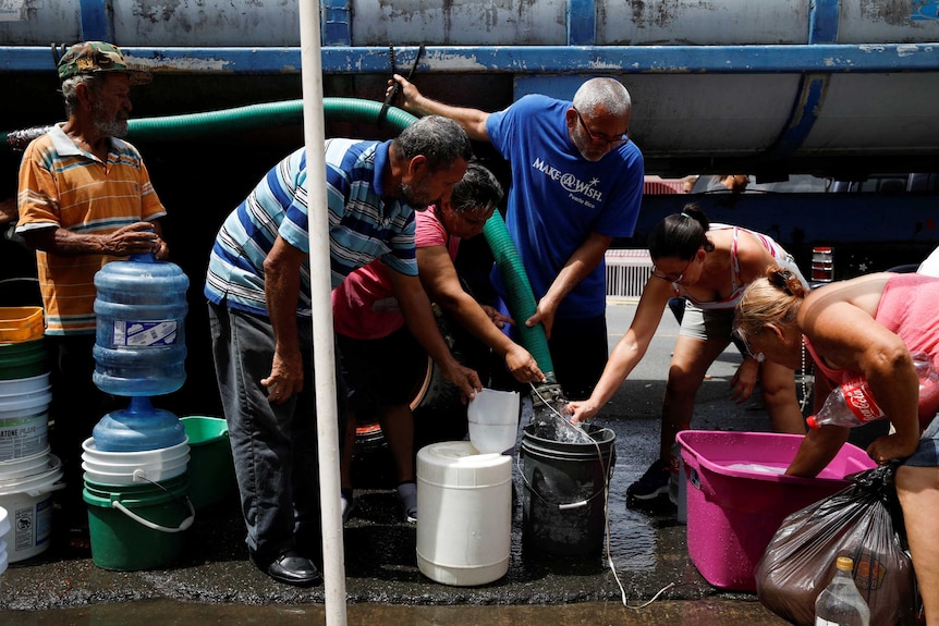 People queue to fill containers with water from a tank truck at an area hit by Hurricane Maria