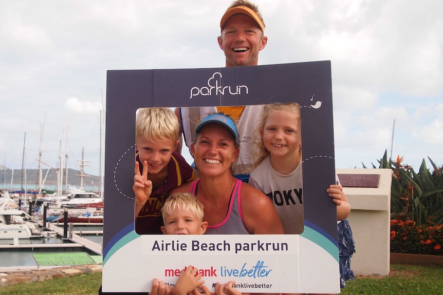 A man, woman and three children pose for a photo inside a cardboard frame.