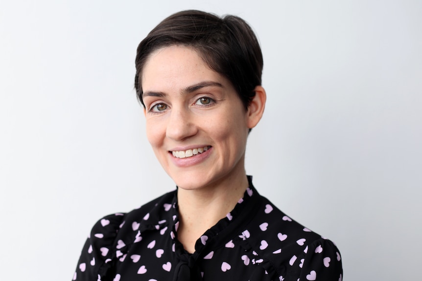 A young woman wearing a black shirt with lilac hearts on it smiles for a professional headshot