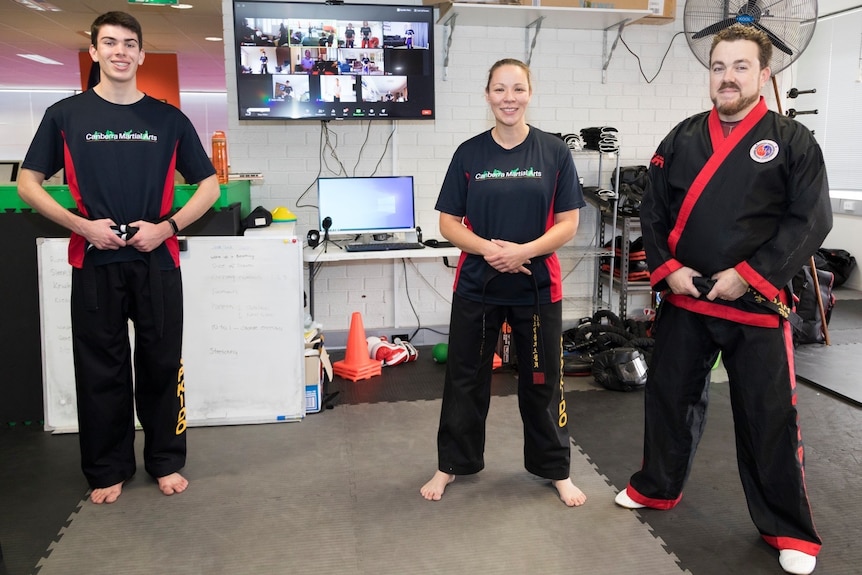 A group of three martial arts instructors standing in front of a screen