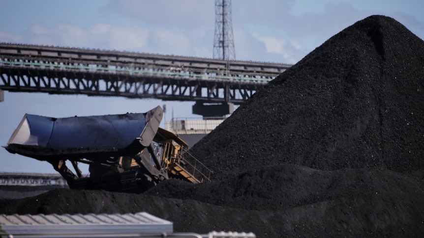 A dozer next to a pile of coal, with conveyor belts in the background