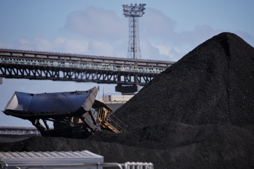 A dozer next to a pile of coal, with conveyor belts in the background