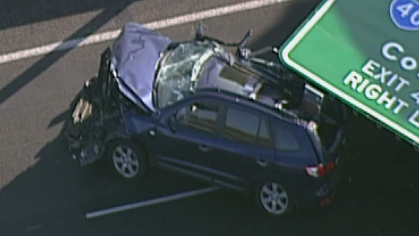 The front of a car is smashed on the Tullamarine Freeway with a road sign lying on the back half of it.