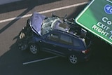 The front of a car is smashed on the Tullamarine Freeway with a road sign lying on the back half of it.