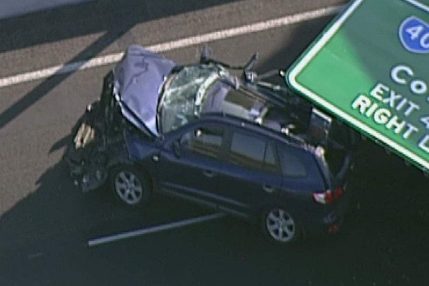 The front of a car is smashed on the Tullamarine Freeway with a road sign lying on the back half of it.