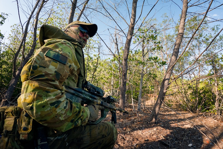 An Australian soldier holding a gun and crouching in the bush.