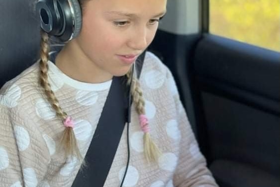 A young girl sits in a car on a computer