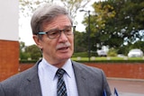 Head and shoulders shot of Mike Nahan wearing a suit, shirt and tie talking to a reporter.