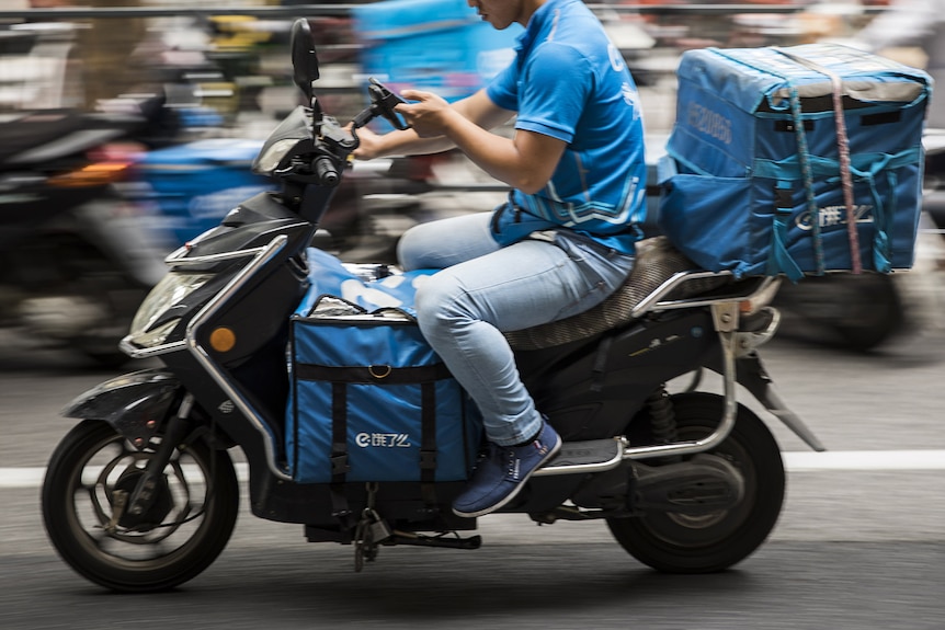 An Ele.me delivery driver on their phone as they drive through traffic.