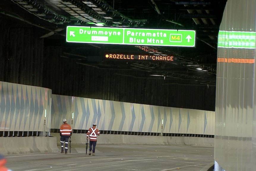 inside view of sydney's Rozelle interchange with two men in high viz walk along 