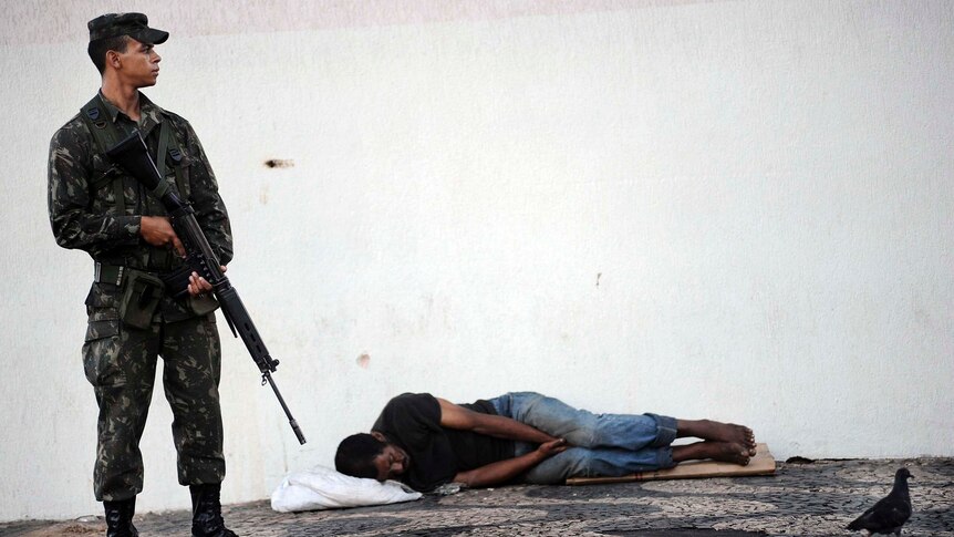 A soldier patrols next to a homeless man sleeping in Salvador, north-east Brazil