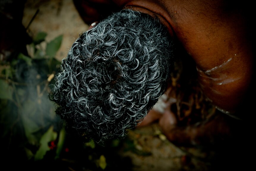 The top of a mans head during a smoking ceremony. 