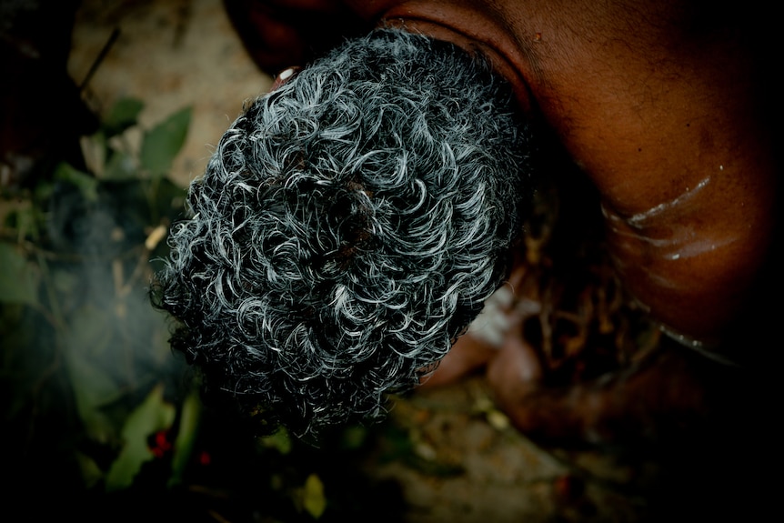 The top of a mans head during a smoking ceremony. 