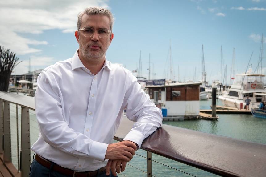 Man wearing a white business shirt leaning against a railing off a pier. 