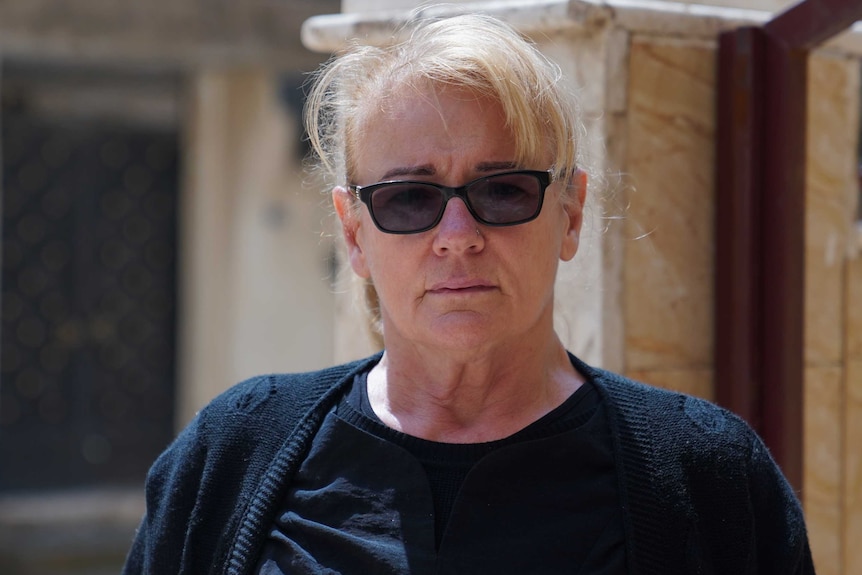 Karen Nettleton wears sunglasses and stands in front of a stone building.