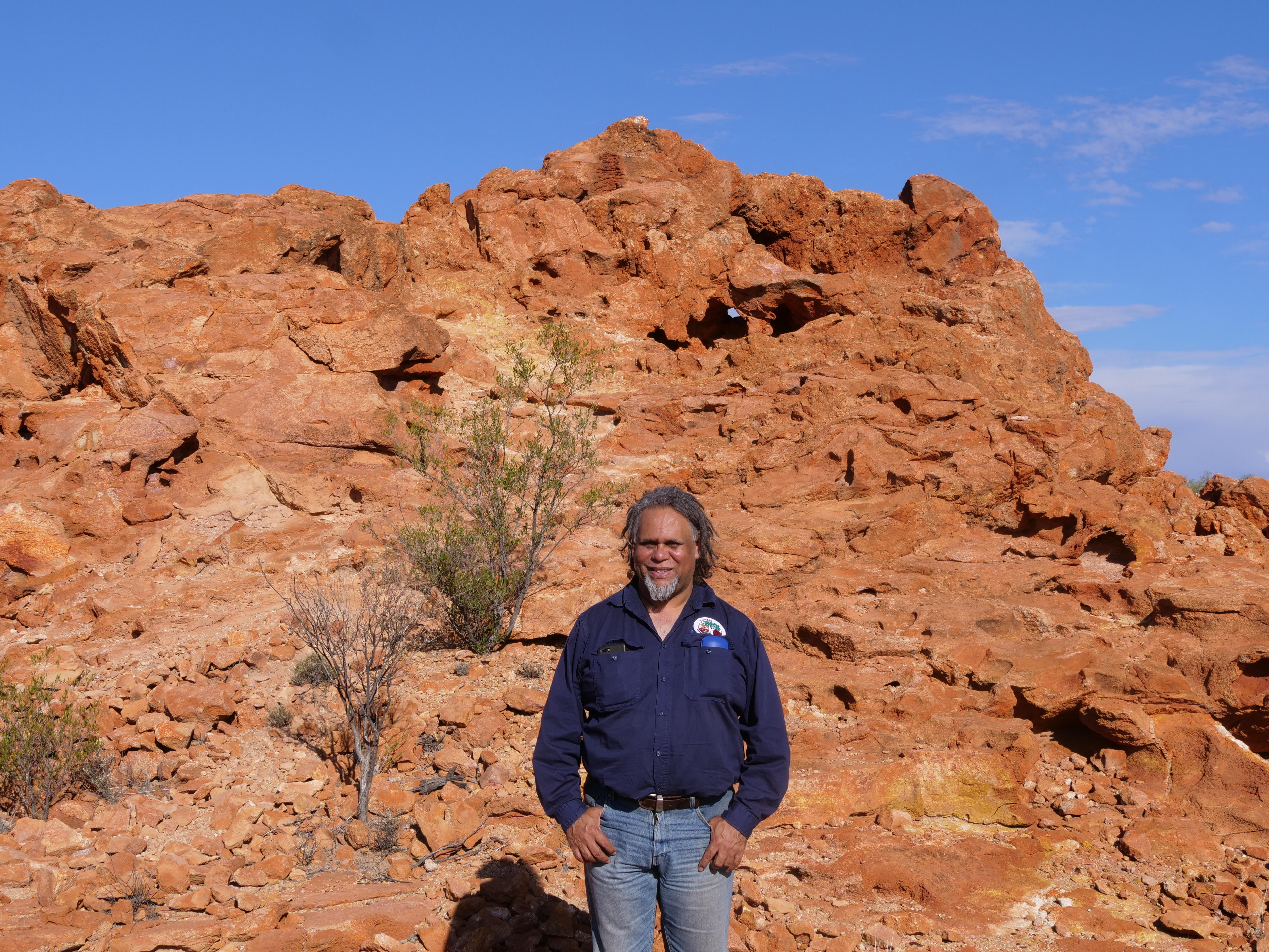 A man in blue shirt stands in front of a rocky outcrop in WA.