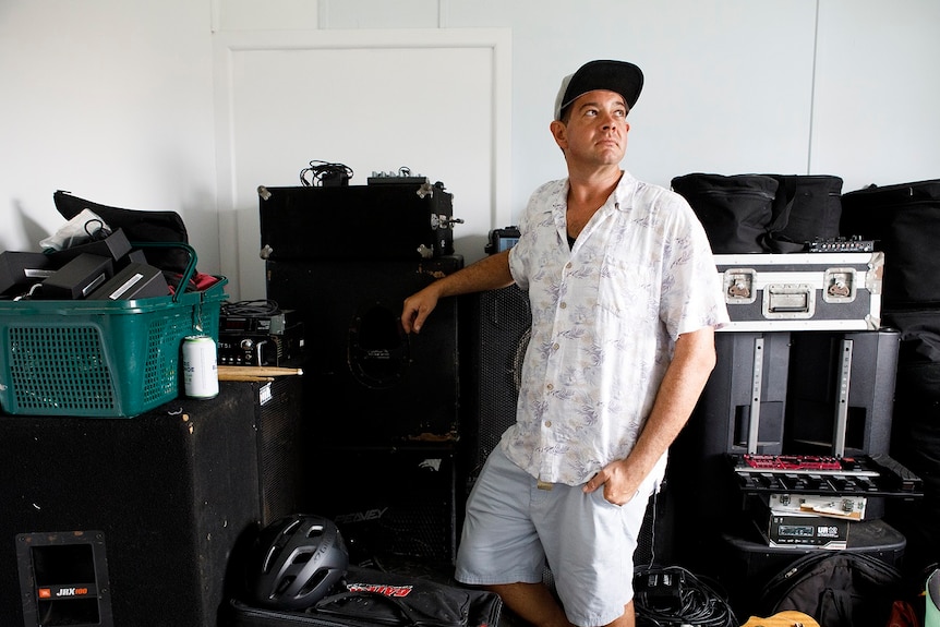 A man leans on cases of musical equipment stacked in a room for a story on share housing.