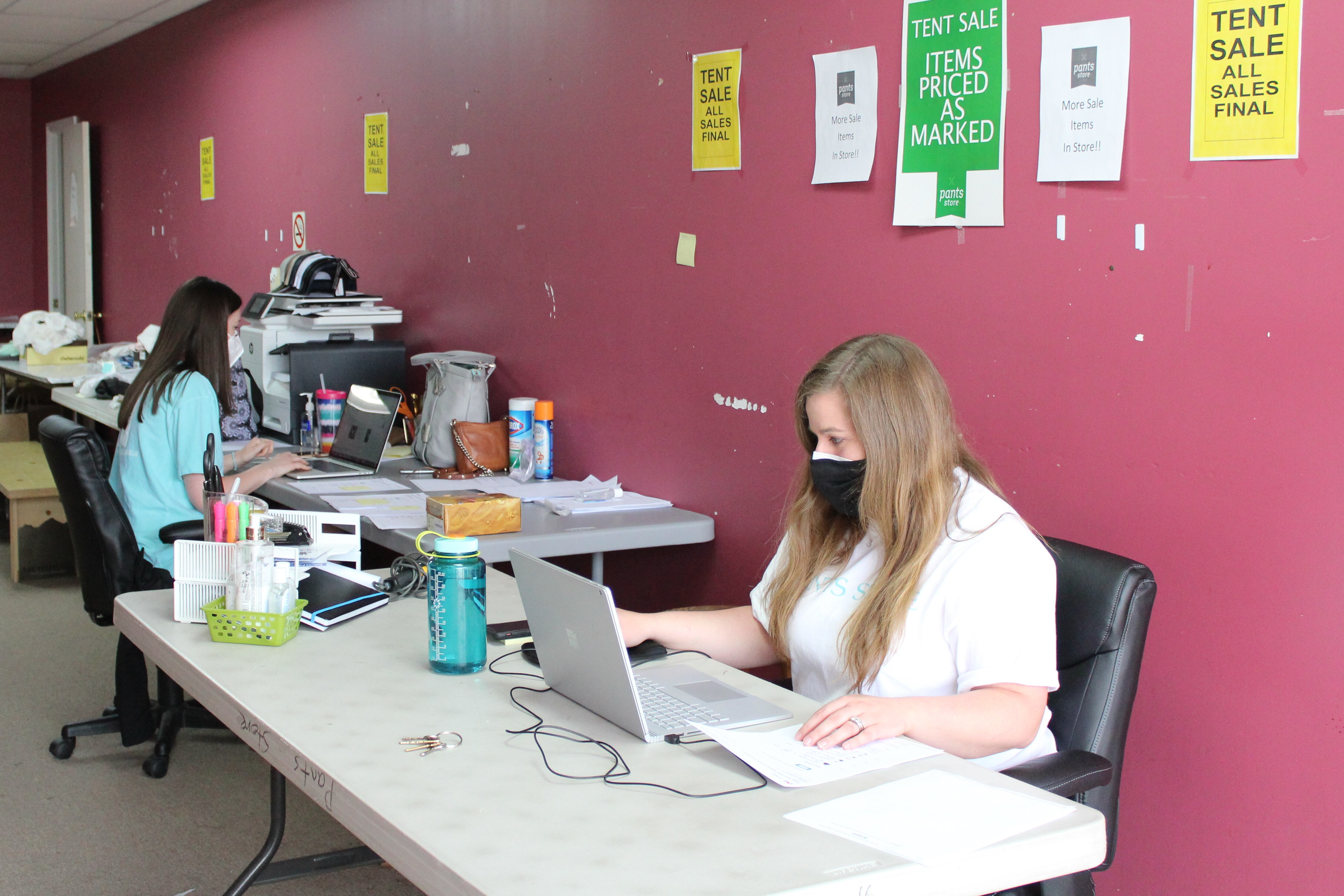 Two women type at computers in a barebones office 