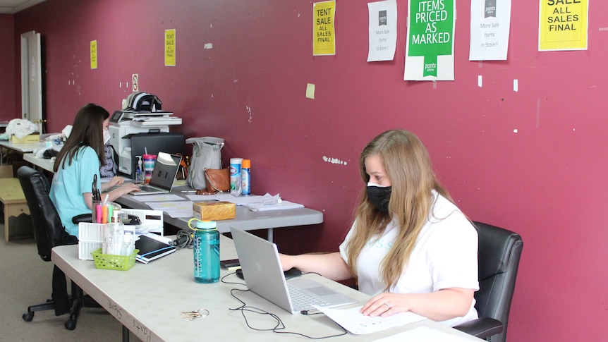 Two women type at computers in a barebones office 