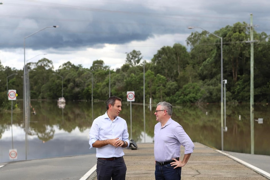 Two men in button up shirts stand on a road covered in water.