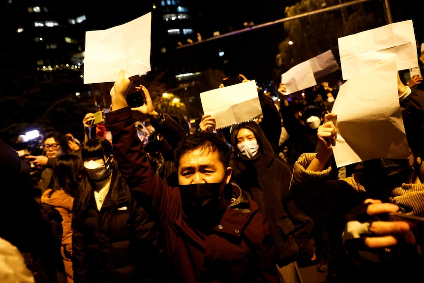 People gather for a vigil and hold white sheets of paper in protest.