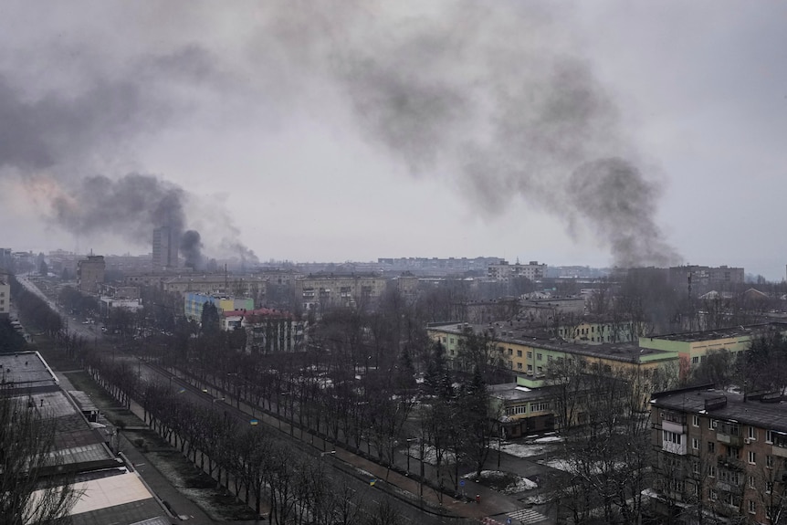 A wide image of a cityscape, showing dark smoke rising from parts of the area.