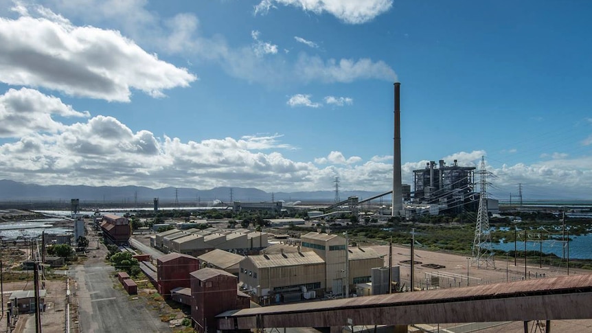 A coal power plant with a tall chimney stack emitting smoke in front of a blue sky and the Flinders Range.