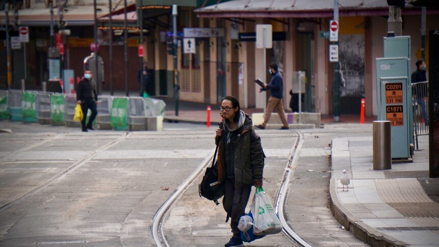 A man carrying plastic bags along a deserted tramway in Sydney lockdown