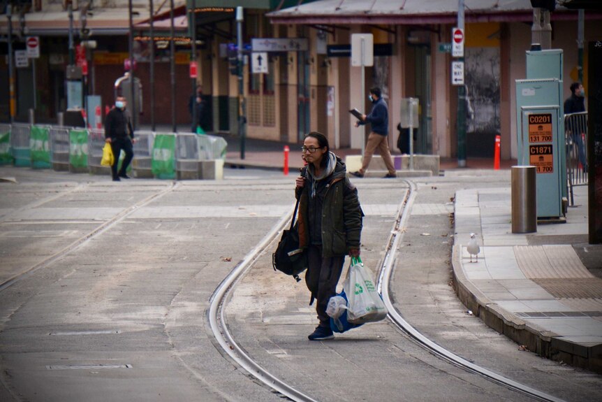 A man carrying plastic bags along a deserted tramway in Sydney lockdown