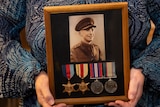 Hands hold a framed photo of a young soldier and four medals.