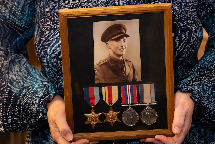 Hands hold a framed photo of a young soldier and four medals.