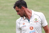 Mitchell Starc looks back at the bottom of his shoe, wearing white cricket clothes