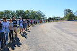 A long queue of people wait in the sun. 
