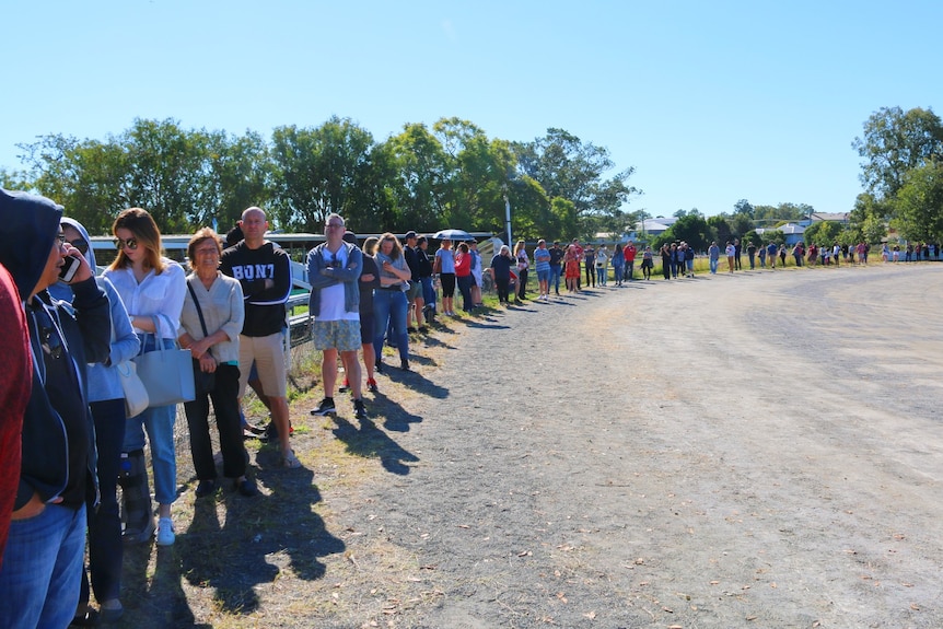 A long queue of people wait in the sun. 