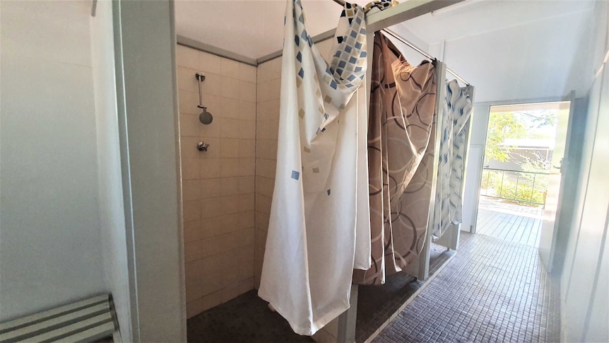 A photo of three showers in a block with shower curtains tied to railing for privacy
